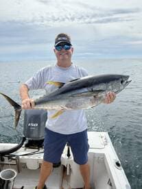 An angler proudly displaying a large Yellowfin Tuna while fishing on a boat in open waters.
