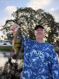 An angler proudly displaying a vibrant Largemouth Bass caught during a peaceful fishing outing on a calm waterway.