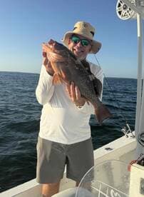 An angler proudly displaying a large Grouper while fishing on a boat in clear waters.