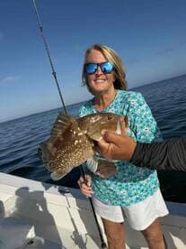 An angler proudly displaying a large Grouper while fishing on a boat, enjoying a sunny day on the water.