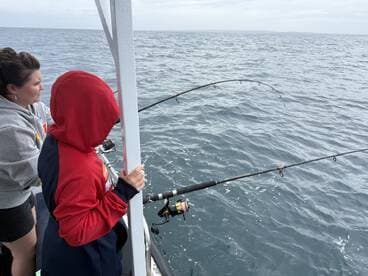 A young angler and an adult are engaged in fishing, with rods bent in anticipation of a catch, showcasing the excitement of deep-sea fishing.
