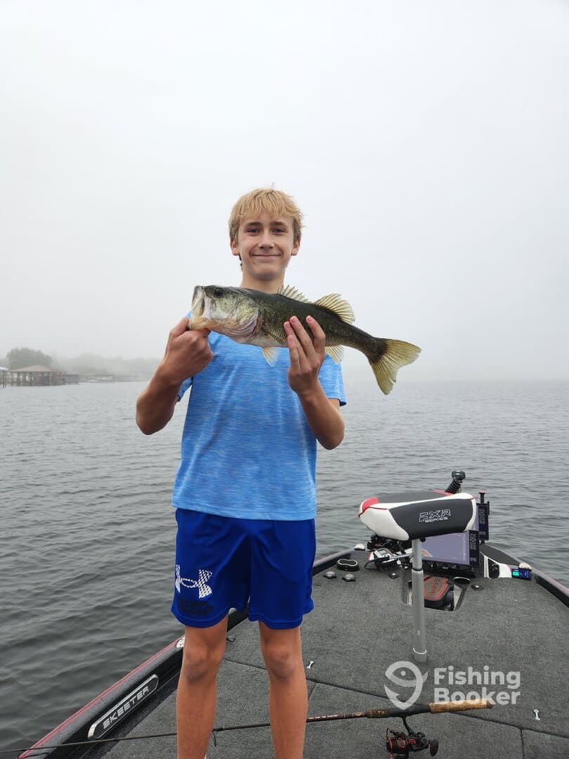 A young angler proudly displaying a large Largemouth Bass while fishing on a foggy lake, showcasing the excitement of a successful catch.
