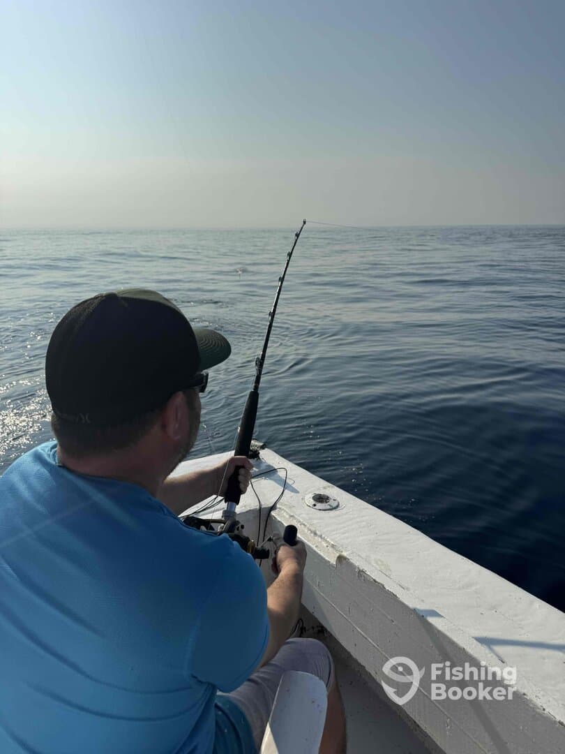 An angler actively reeling in a fish while fishing on a calm ocean, showcasing the excitement of the catch.
