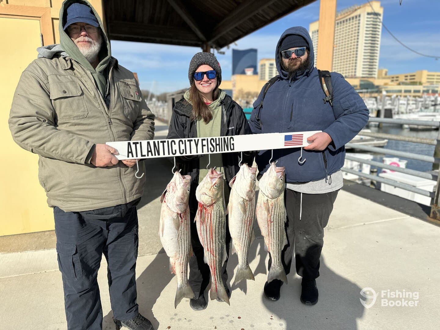 Three anglers proudly displaying their catch of striped bass at the marina in Atlantic City, showcasing a successful fishing trip.