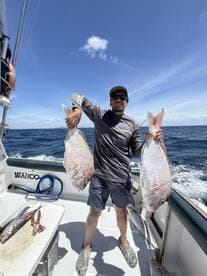 Angler proudly displaying two large Snapper caught during a deep-sea fishing trip aboard the Wahoo.