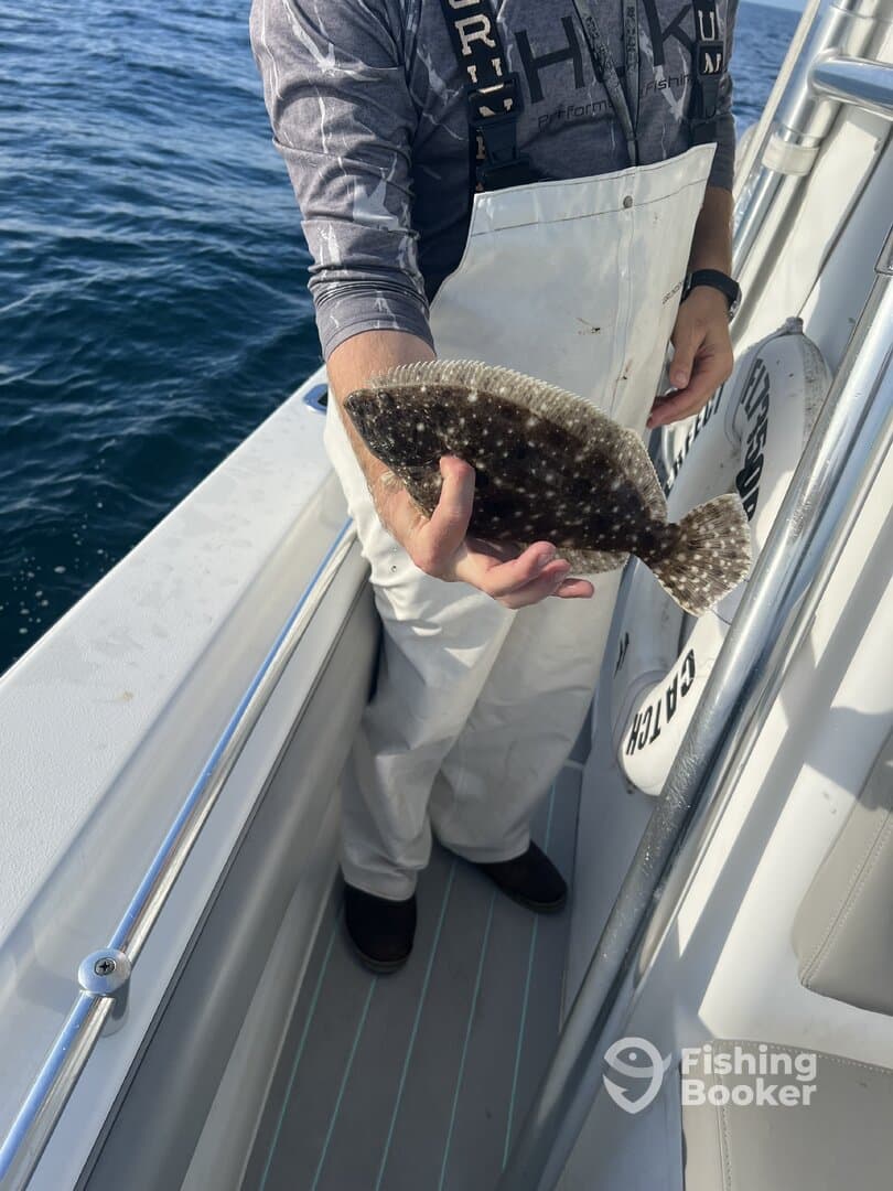 Angler displaying a Flounder while standing on the deck of a fishing boat, showcasing a successful catch during a deep-sea fishing trip.
