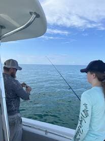 A young angler watches as an adult prepares a bait while fishing on a boat in calm waters, showcasing a shared fishing experience.