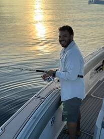 A smiling angler casting a line from a modern fishing boat during a serene sunset, showcasing the peaceful fishing environment.