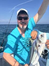 An angler proudly displaying a large fish while fishing offshore, showcasing a sunny day on the water.