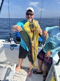 An angler proudly displaying a vibrant Mahi Mahi while fishing offshore, showcasing a successful day on the water.