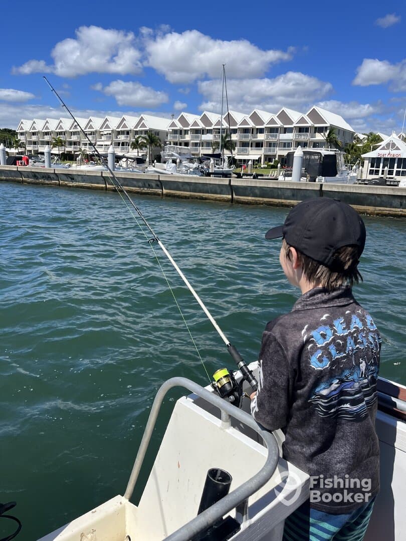 A young angler casting a line from a boat in a marina setting, with waterfront accommodations in the background.