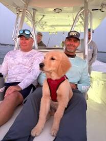 Group of anglers enjoying a day on the boat, accompanied by a golden retriever puppy, showcasing a relaxed fishing atmosphere.