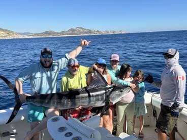 A family celebrates a successful catch of a large Marlin while fishing off the coast, showcasing their excitement and teamwork.