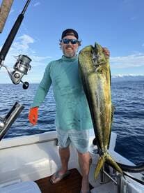 Angler proudly displaying a large Mahi Mahi while fishing on a boat in open waters.