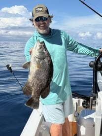 An angler proudly displaying a large Black Drum while fishing on a calm day at sea.