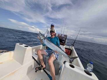 Angler proudly displaying a large Barracuda while fishing from a small boat in open waters.