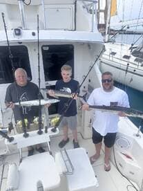 Three anglers proudly displaying their catch of Barracuda aboard a sportfishing boat, showcasing a successful day on the water.