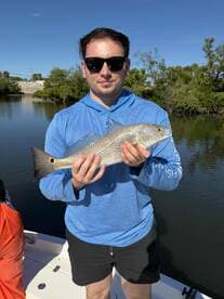 Angler holding a Silver Drum while fishing in a calm waterway, showcasing a successful catch during a sunny day.