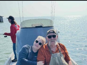 A couple enjoying a relaxing moment on the boat, surrounded by calm waters, with a fishing rod in the background.