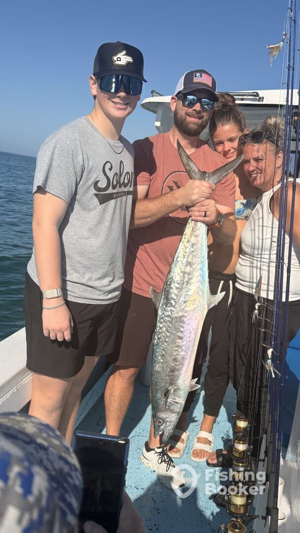 A group of anglers proudly displaying a large King Mackerel aboard a fishing charter, enjoying a sunny day on the water.