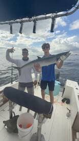 Two anglers proudly displaying a large King Mackerel aboard a fishing boat, enjoying a successful day on the water.