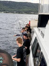 A group of anglers actively fishing from a charter boat, surrounded by scenic coastal views and mountainous terrain.