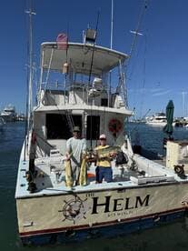 Two anglers proudly displaying their catch of Mahi Mahi on the deck of 'The Helm' in Key West, showcasing a successful day of fishing.
