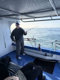 A fisherman actively reeling in a catch aboard a fishing charter, with calm waters in the background.