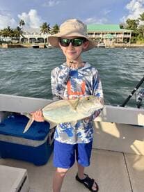 A young angler proudly displaying a large fish while fishing from a boat, with a scenic waterfront in the background.