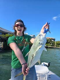 Excited young angler holding a large Jack Crevalle while fishing from a boat in a coastal area.