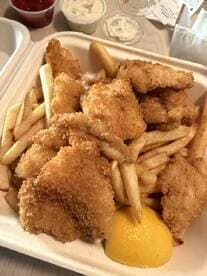 A plate of fried fish and fries, accompanied by dipping sauces and a lemon wedge.