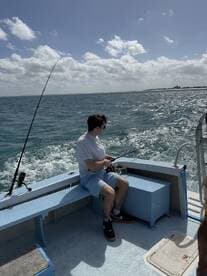 A young angler casting a line while enjoying a day of fishing on a boat in clear blue waters.