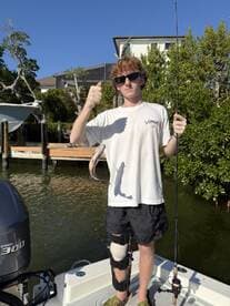 A young angler proudly displaying a caught fish while fishing from a boat in a scenic waterway.