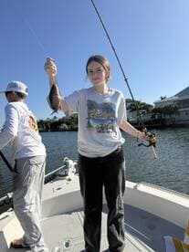 A young angler proudly displaying a caught fish while fishing from a boat in a scenic waterway.