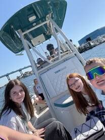 A group of young anglers enjoying their time on a boat, showcasing the interior seating area with a sunny waterfront backdrop.