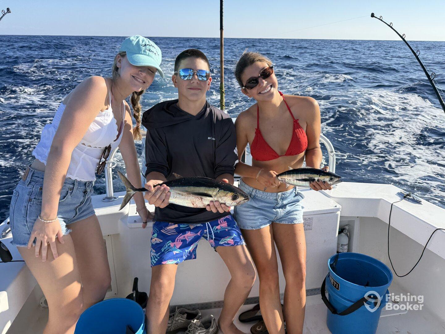 Three young anglers proudly displaying their catch of small tuna while enjoying a day on the water.