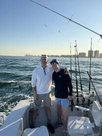 A father and son enjoying a fishing trip on a boat, with a scenic view of the coastline in the background.