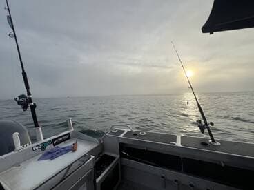 Interior view of a fishing boat with rods ready for action, set against a serene sunrise over the water.