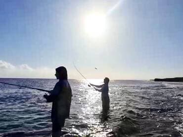 Two anglers casting lines into the ocean during a sunny day, showcasing the excitement of fishing in a coastal environment.