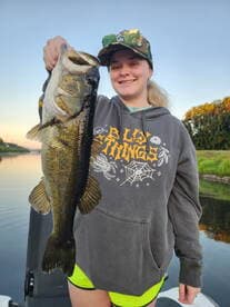 Young angler proudly holding a large Largemouth Bass while fishing on a calm waterway.