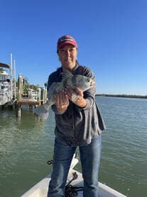 Angler proudly displaying a large striped bass while standing on a boat in calm waters.