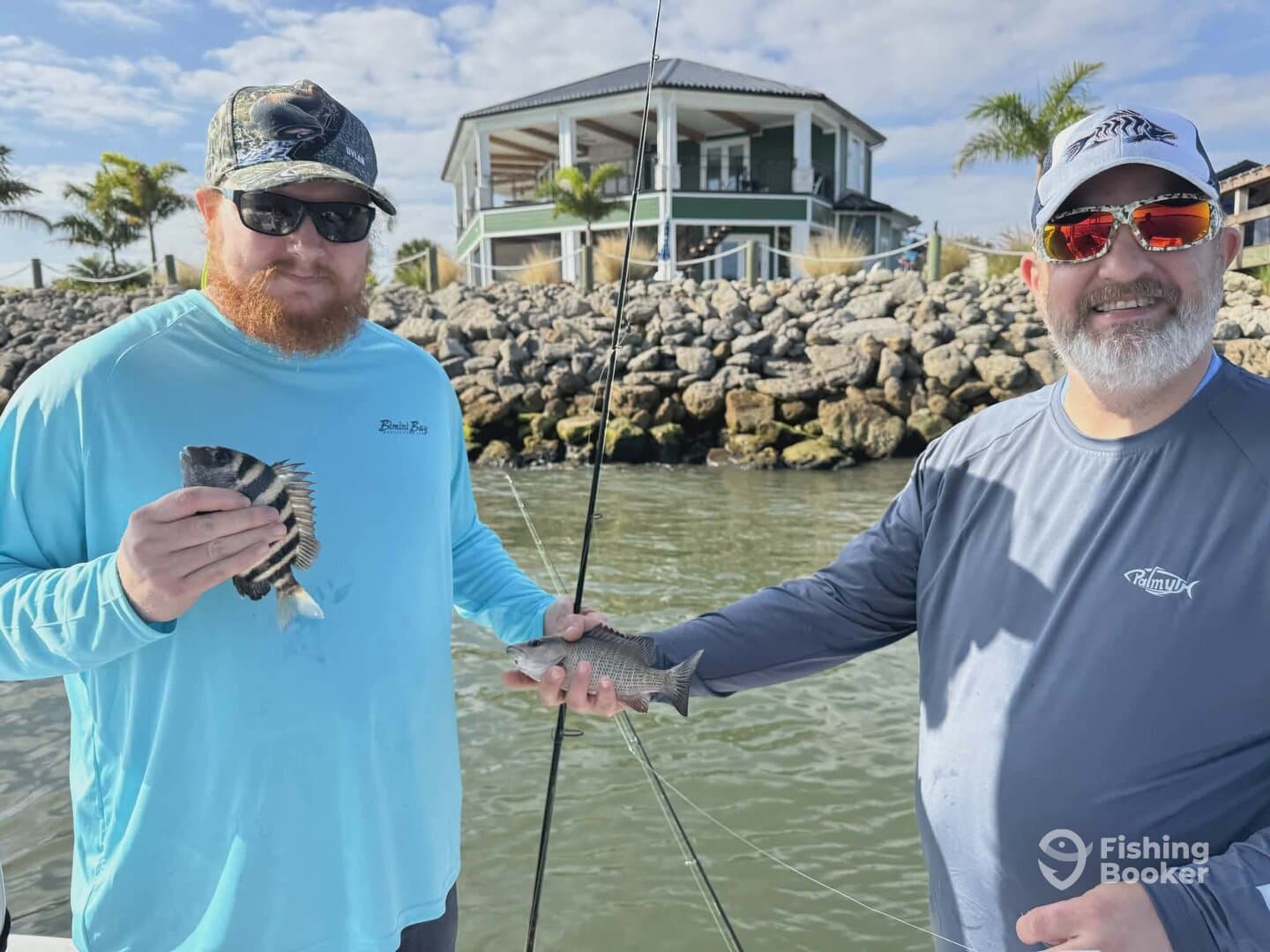 Two anglers proudly displaying their catch of striped fish while fishing near a rocky shoreline.