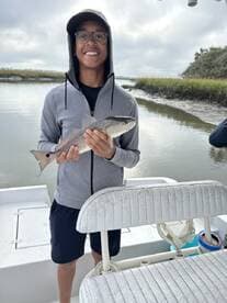 A young angler proudly holding a Redfish while fishing in a scenic estuary.