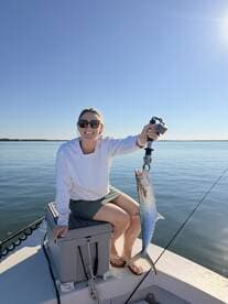 A smiling angler holding a large Spanish Mackerel while sitting on a boat, enjoying a sunny day on the water.