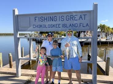 A family proudly displaying their catch of fish in front of a sign at Chokoloskee Island, Florida, showcasing a fun fishing trip.