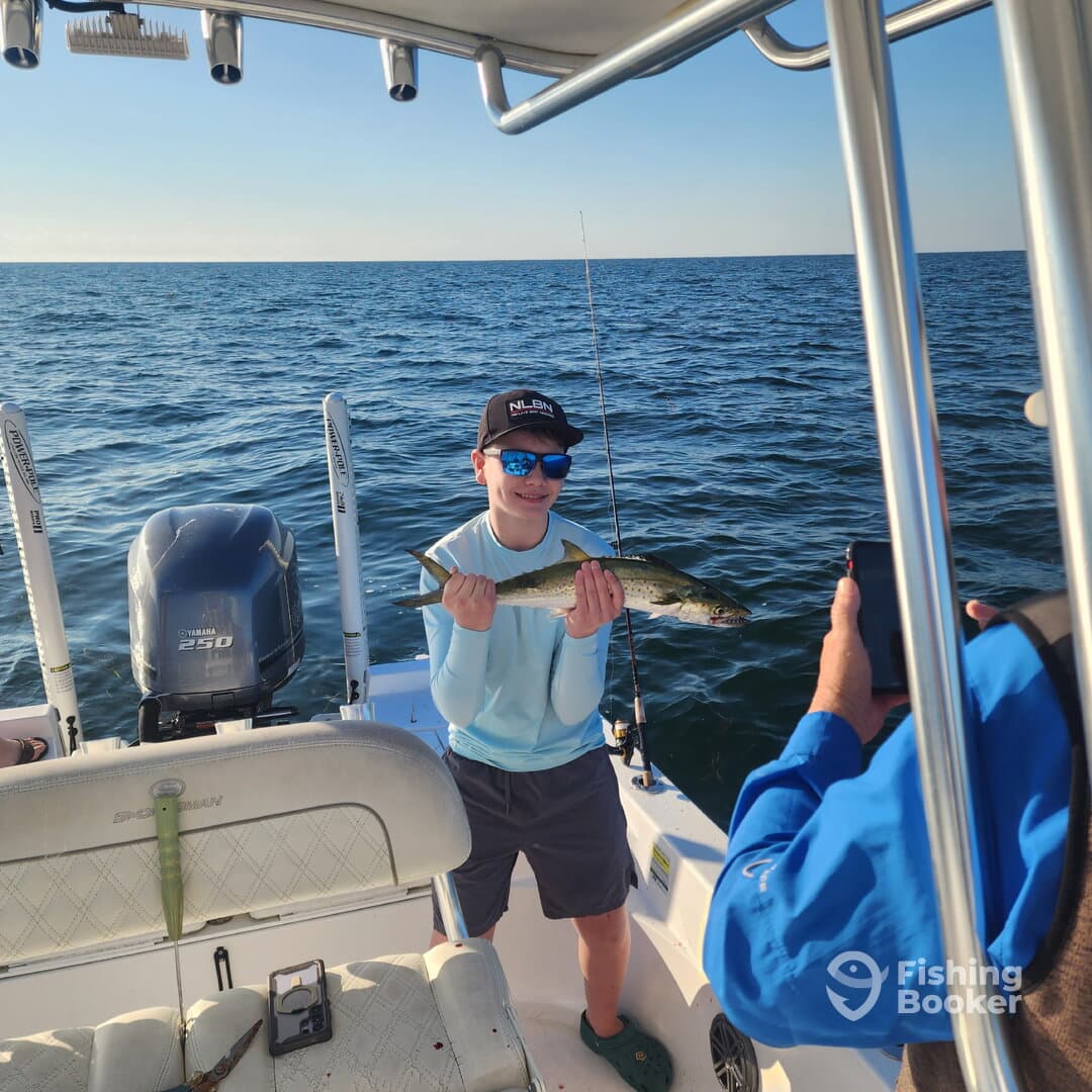 A young angler proudly displaying a caught fish while fishing on a boat in open waters.