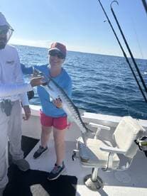 A smiling angler proudly displays a large Barracuda while fishing on a boat in clear blue waters.