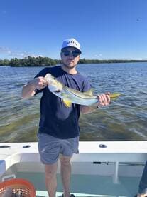 Angler proudly displaying a large Snook while fishing in a scenic coastal environment.