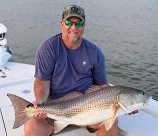 Angler proudly displaying a large striped bass while seated on a boat, showcasing a successful fishing trip.