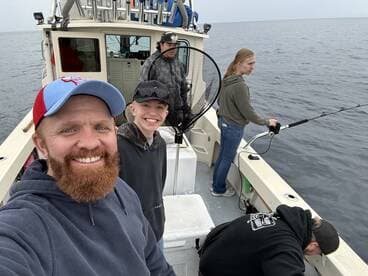A group of anglers enjoying a fishing trip on a boat, with one person actively reeling in a line while others prepare for their catch.